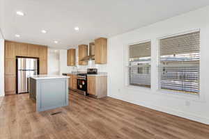 Kitchen with a kitchen island, light wood-type flooring, stainless steel appliances, and wall chimney range hood