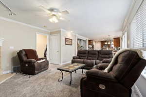 Carpeted living room with track lighting, ceiling fan, and ornamental molding