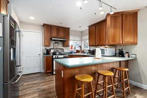 Kitchen with exhaust hood, a breakfast bar area, dark hardwood / wood-style floors, kitchen peninsula, and stainless steel appliances