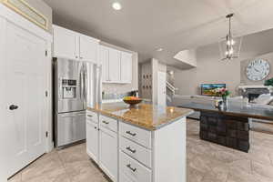 Kitchen featuring white cabinets, stainless steel fridge, a center island, and a stone fireplace