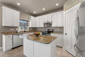 Kitchen featuring stainless steel appliances, light tile patterned floors, a kitchen island, stone countertops, and white cabinets