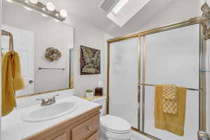 Bathroom with lofted ceiling with skylight, a textured ceiling, toilet, a shower with door, and vanity