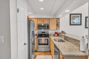 Kitchen featuring kitchen peninsula, appliances with stainless steel finishes, light stone counters, sink, and light hardwood / wood-style floors