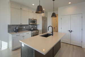 Kitchen with backsplash, high quality appliances, sink, and a center island with sink