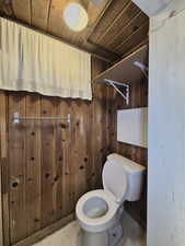 Bathroom with toilet, wood ceiling, and wooden walls