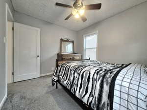 Carpeted bedroom with ceiling fan and a textured ceiling