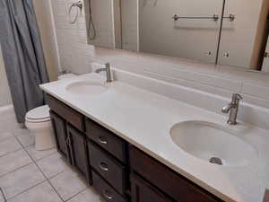 Full bathroom with tasteful backsplash, vanity, shower / bathtub combination with curtain, tile patterned flooring, and toilet