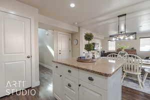 Kitchen featuring light stone counters, dark wood-type flooring, white cabinets, a center island, and hanging light fixtures