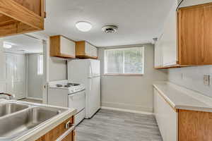 Kitchen with white cabinets, light hardwood / wood-style floors, white range, and sink