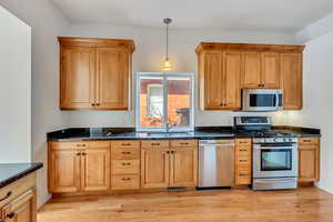 Kitchen with appliances with stainless steel finishes, dark stone counters, sink, decorative light fixtures, and light hardwood / wood-style flooring