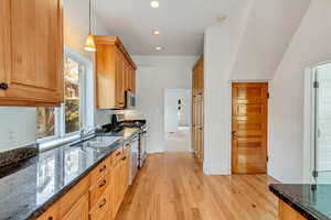 Kitchen featuring dark stone countertops, sink, stainless steel appliances, and light wood-type flooring