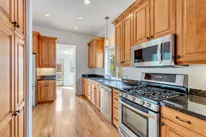 Kitchen featuring dark stone counters, sink, hanging light fixtures, light wood-type flooring, and appliances with stainless steel finishes