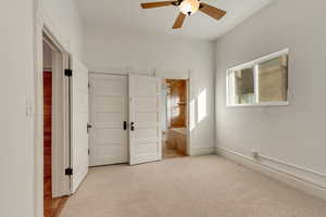 Unfurnished bedroom featuring a closet, light colored carpet, ensuite bath, and ceiling fan