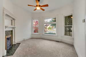 Unfurnished living room featuring ceiling fan, dark carpet, and a brick fireplace