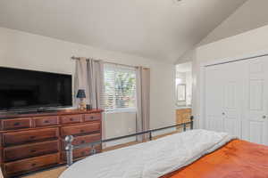 Bedroom with vaulted ceiling, light colored carpet, ensuite bath, and a closet