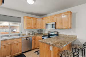 Kitchen with sink, a breakfast bar area, light tile patterned floors, kitchen peninsula, and stainless steel appliances