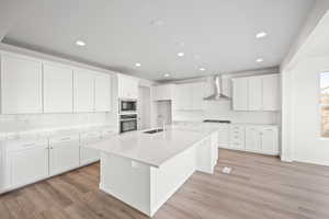 Kitchen with a kitchen island with sink, white cabinets, oven, wall chimney exhaust hood, and built in microwave