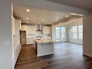 Kitchen featuring stainless steel oven, a kitchen island with sink, an inviting chandelier, wall chimney exhaust hood, and white cabinetry