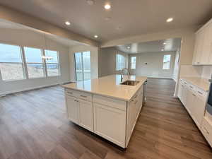 Kitchen with sink, dark wood-type flooring, an island with sink, a chandelier, and white cabinets