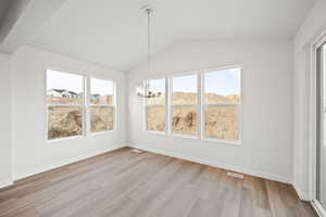 Unfurnished dining area with vaulted ceiling, light hardwood / wood-style floors, and an inviting chandelier