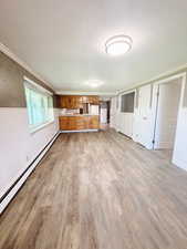 Unfurnished living room with light hardwood / wood-style floors, crown molding, baseboard heating, and wooden walls