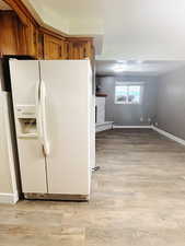 Kitchen featuring white refrigerator with ice dispenser, light wood-type flooring, and a baseboard heating unit