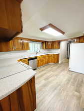 Kitchen with dishwasher, sink, white fridge, light hardwood / wood-style floors, and exhaust hood