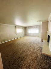 Carpeted empty room featuring a fireplace, a healthy amount of sunlight, and a textured ceiling