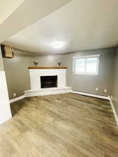 Unfurnished living room with hardwood / wood-style floors, a baseboard radiator, and a brick fireplace