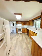 Kitchen with kitchen peninsula, sink, white appliances, and light hardwood / wood-style flooring