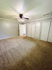 Unfurnished bedroom featuring carpet flooring, ornamental molding, ceiling fan, and multiple closets