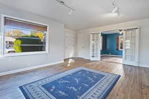 Spare room featuring french doors, track lighting, plenty of natural light, and hardwood / wood-style flooring