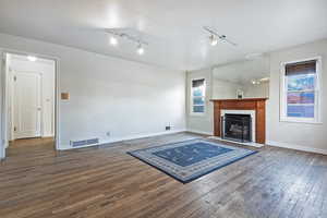 Unfurnished living room featuring rail lighting, dark hardwood / wood-style floors, and a fireplace