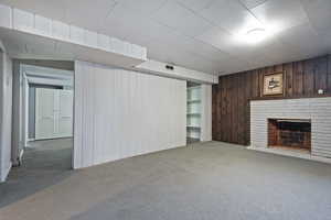 Unfurnished living room featuring wood walls, light colored carpet, and a fireplace