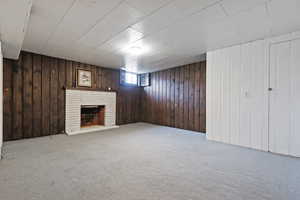 Basement featuring wood walls, light colored carpet, and a brick fireplace