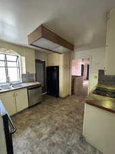 Kitchen featuring tasteful backsplash, cream cabinets, sink, and black appliances