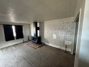 Unfurnished living room featuring a wood stove, wooden walls, and carpet floors