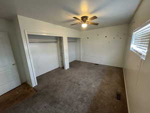 Unfurnished bedroom featuring dark colored carpet, ceiling fan, and multiple closets