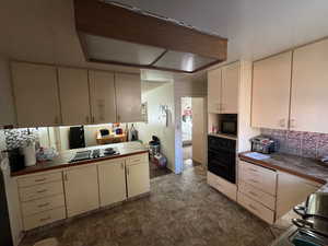 Kitchen with black appliances, tile counters, decorative backsplash, and cream cabinets