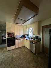 Kitchen with oven, sink, stainless steel dishwasher, decorative backsplash, and cream cabinetry