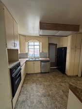 Kitchen featuring black refrigerator, sink, stainless steel dishwasher, cream cabinetry, and wall oven