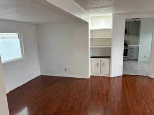 Unfurnished living room with hardwood / wood-style floors, built in features, and a textured ceiling