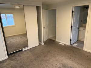 Unfurnished bedroom with ensuite bathroom, dark carpet, and a closet