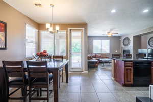 Tiled dining area featuring a textured ceiling, plenty of natural light, a fireplace, and ceiling fan with notable chandelier