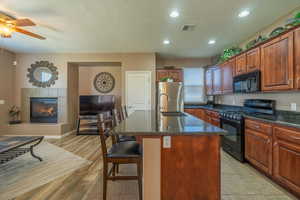 Kitchen with a textured ceiling, black appliances, a fireplace, light hardwood / wood-style floors, and an island with sink