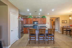 Kitchen featuring a kitchen breakfast bar, a textured ceiling, sink, a center island with sink, and stainless steel refrigerator