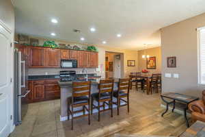 Kitchen with an island with sink, a textured ceiling, decorative light fixtures, a kitchen bar, and black appliances