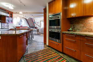 Kitchen with sink, hanging light fixtures, stainless steel double oven, backsplash, and light tile patterned floors