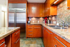 Kitchen featuring tasteful backsplash, light stone countertops, sink, and stainless steel built in refrigerator