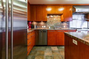 Kitchen featuring decorative backsplash, sink, exhaust hood, and appliances with stainless steel finishes